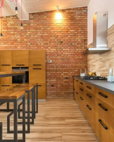 Modern kitchen with wooden cabinets, exposed brick wall, and a cooking area with a gas stove and range hood.